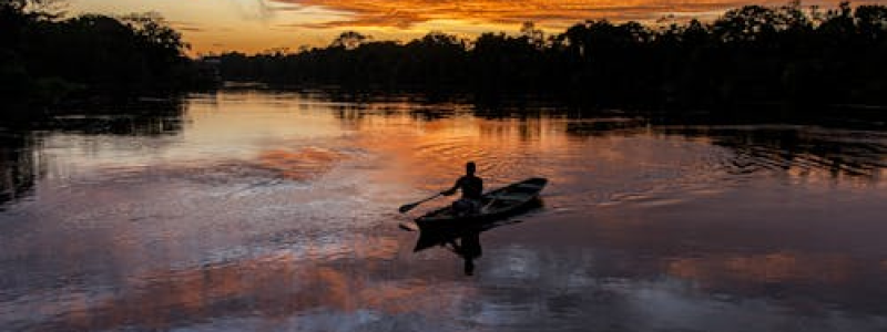 Pescador em canoa no Rio Amazonas ao pôr do sol com céu alaranjado refletindo na água